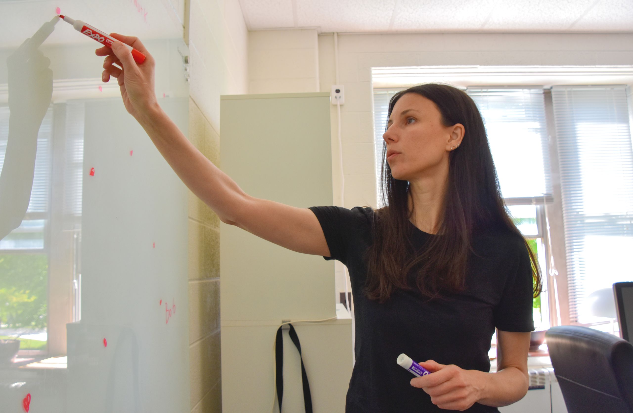 Dr. Sophia Economou writing on a white board with a red marker in a classroom.