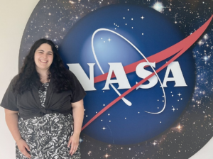 Dark-haired female scientist stands in front of the NASA logo