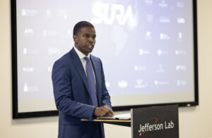 A man stands at a podium and talks to a room of people sitting at tables.